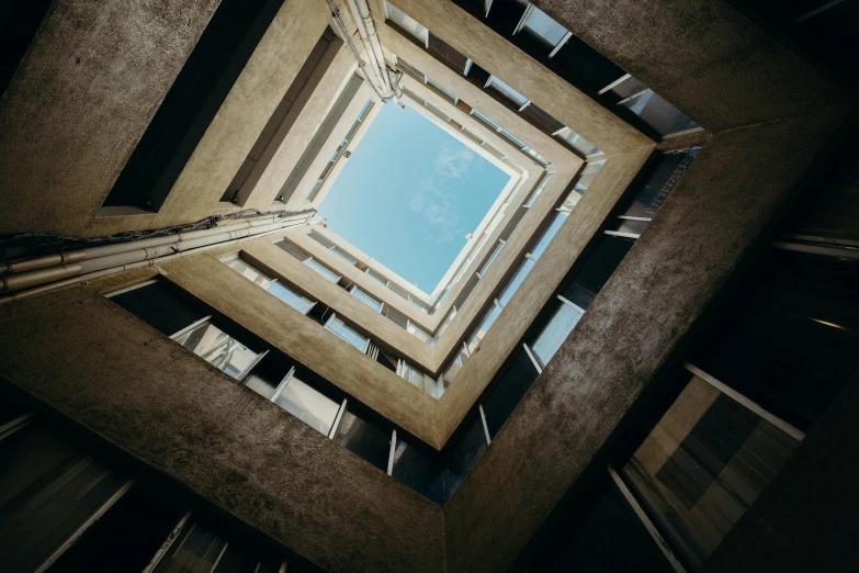 the inside of a building looking up at the sky, an album cover, inspired by Alexander Rodchenko, unsplash contest winner, brutalism, sunken square, natural light outside, high view, a wide open courtyard in an epic