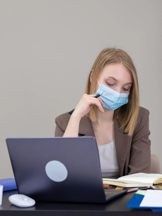 a woman sitting at a desk with a laptop wearing a face mask, a picture, trending on pexels, happening, protruding chin, thumbnail, profile pic, medicine