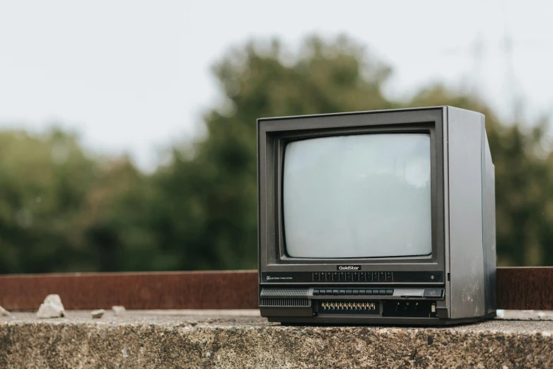a small television sitting on top of a cement wall, a cartoon, unsplash, 1 9 8 0 s computers, politics, tvp, tv series
