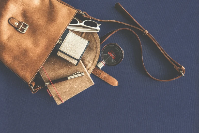 a brown purse sitting on top of a blue surface, a still life, trending on pexels, small vials and pouches on belt, scrapbook, leather and suede, navy