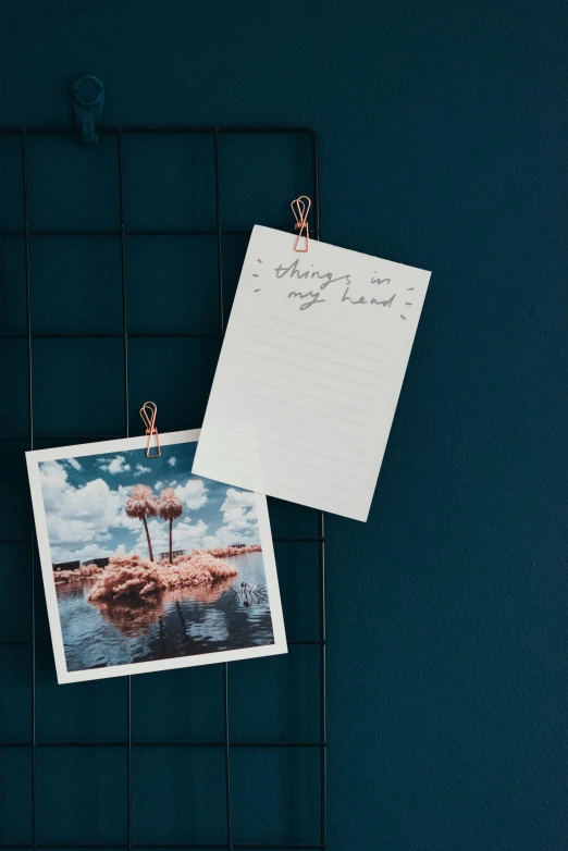 a picture hanging on a wall with a note attached to it, a polaroid photo, inspired by Wilhelm Marstrand, unsplash, copper details, holding notebook, dreamy mood, two hang