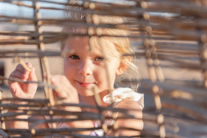 a little girl that is inside of a cage, a picture, by Lilia Alvarado, unsplash, conceptual art, wicker art, having fun in the sun, medium close up portrait, near the beach