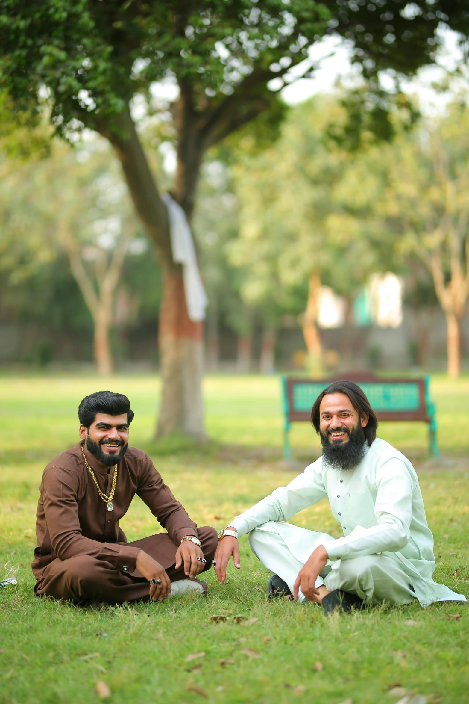 a couple of men sitting on top of a lush green field, wearing a kurta, in a park, profile image, portrait image