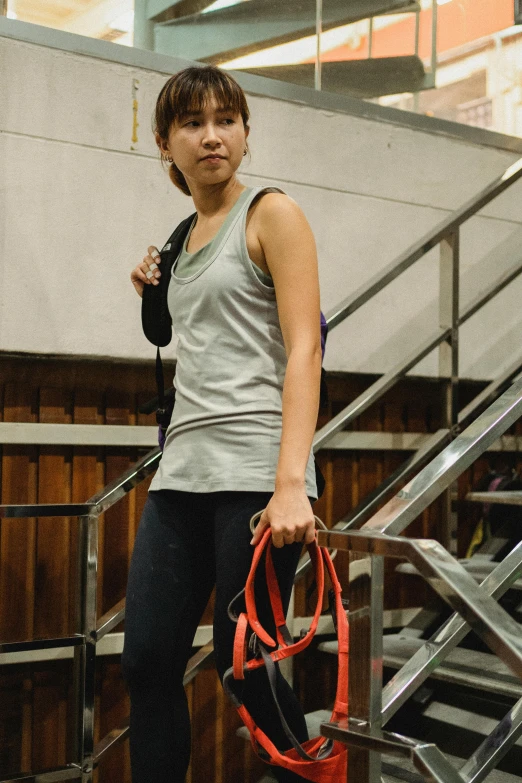 a woman standing on a set of stairs holding a bag, pexels contest winner, chun li at the gym, harnesses, wearing : tanktop, grey