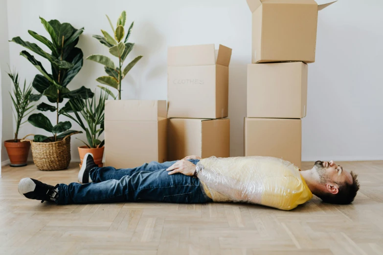a man laying on the floor surrounded by boxes, inspired by Sarah Lucas, pexels contest winner, hurufiyya, hungover, covered in plants, sydney hanson, promotional image