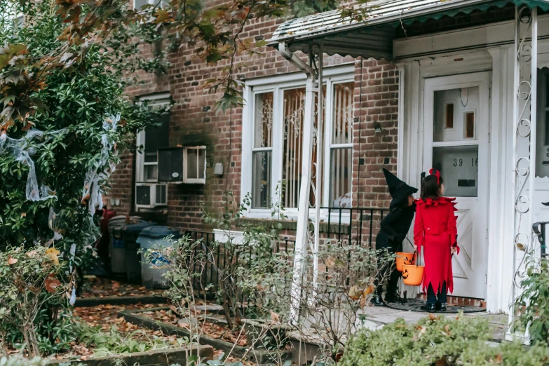 a couple of people that are standing in front of a house, by Julia Pishtar, pexels, trick or treat, brooklyn, red hoods, families playing