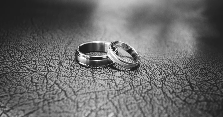 two wedding rings sitting on top of a leather surface, a black and white photo, pixabay, asphalt and metal, wearing robes of silver, cracks, uploaded