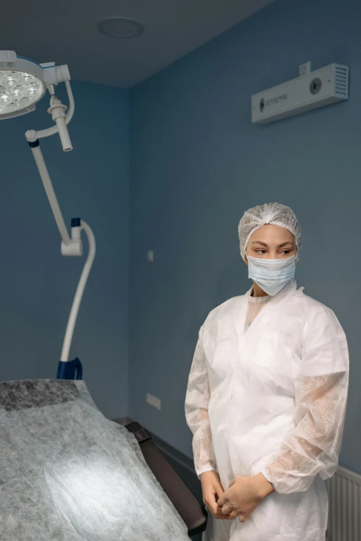a man in a lab coat standing in front of an operating light, by Adam Marczyński, pexels contest winner, photo of a woman, surgery theatre, mongolia, gray
