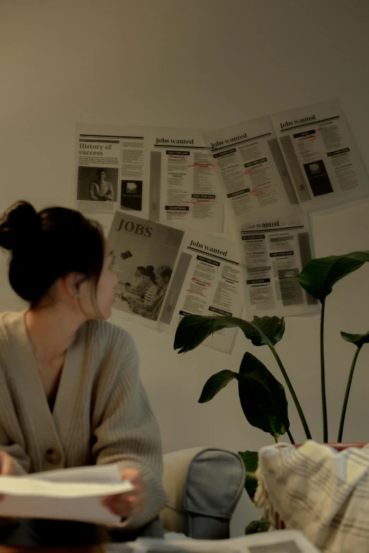 a woman sitting on a couch reading a book, a picture, by Jang Seung-eop, unsplash contest winner, happening, newspaper clippings, on a desk, low quality photo, posters on the wall