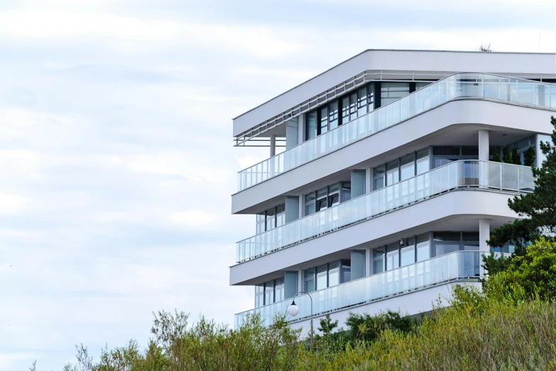 a tall white building sitting on top of a lush green hillside, inspired by Tadao Ando, unsplash, bauhaus, beachfront, balcony, grey, ten flats