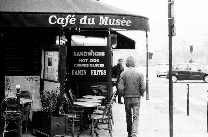 a man walking down the sidewalk in front of a cafe, a photo, inspired by Henri Cartier-Bresson, muse, snacks, a cozy, at the museum