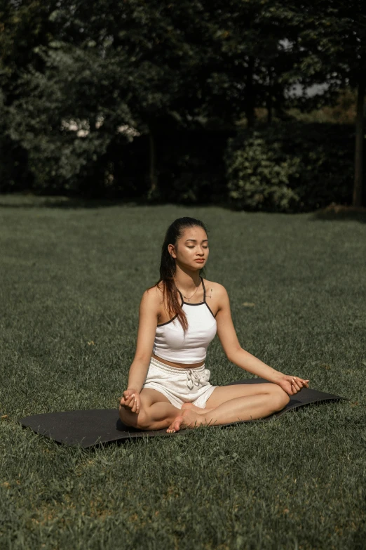 a woman sitting on a yoga mat in a park, a portrait, pexels contest winner, renaissance, young asian woman, padmasana, low quality photo, su fu