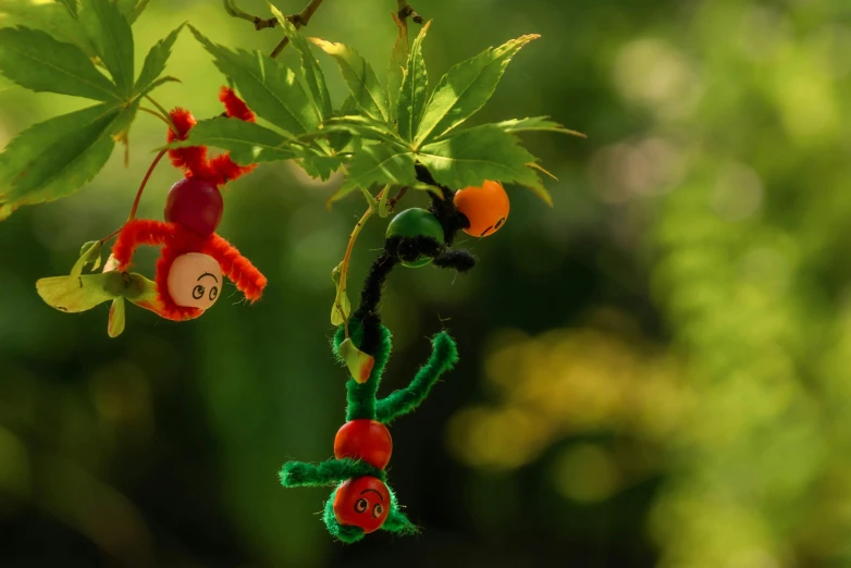 a stuffed animal hanging from a tree branch, inspired by Alexander Stirling Calder, pexels contest winner, process art, jungle fruit, worms, bright green dark orange, toys figures