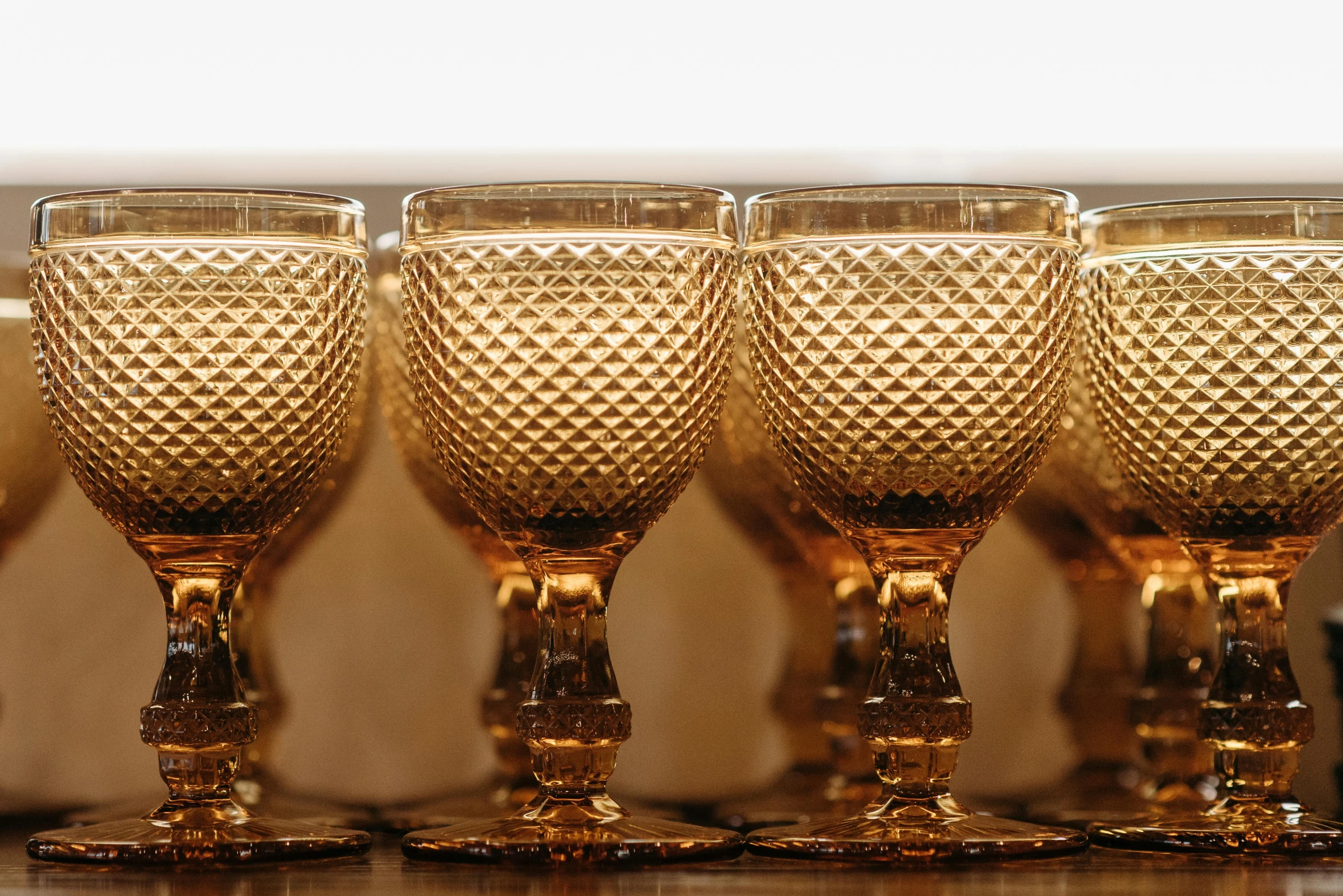 a group of wine glasses sitting on top of a wooden table, an album cover, pexels, renaissance, ocher, highly detailed textured 8k, faceted, in a row