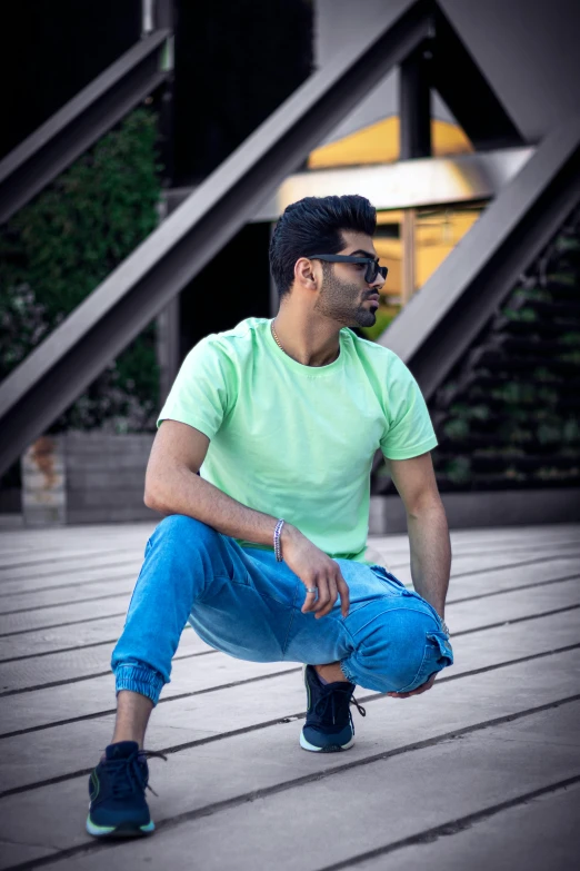 a man sitting on top of a wooden floor, inspired by Manjit Bawa, pexels contest winner, hurufiyya, pastel green, wearing pants and a t-shirt, lgbtq, ( ( ( colorful ) ) )