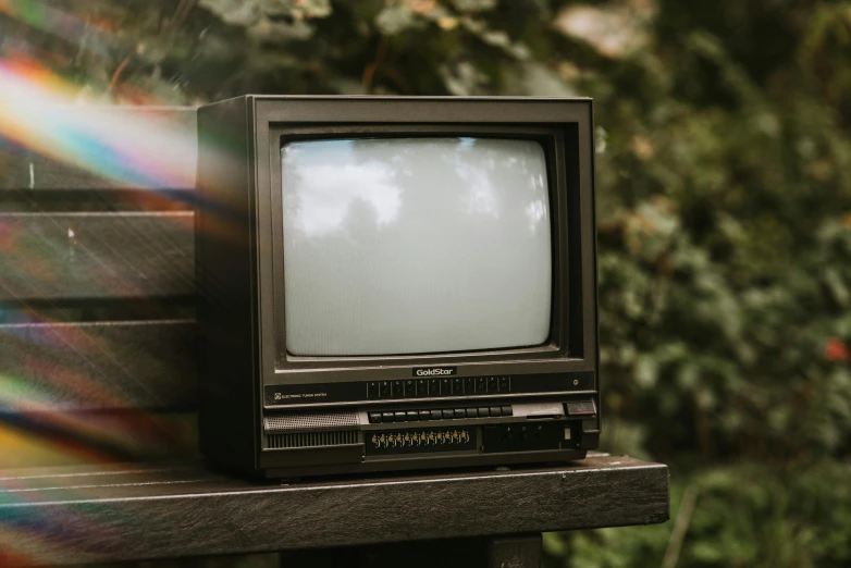 a small television sitting on top of a wooden bench, unsplash, 1 9 8 0 s tech, politics, a green, looking outside