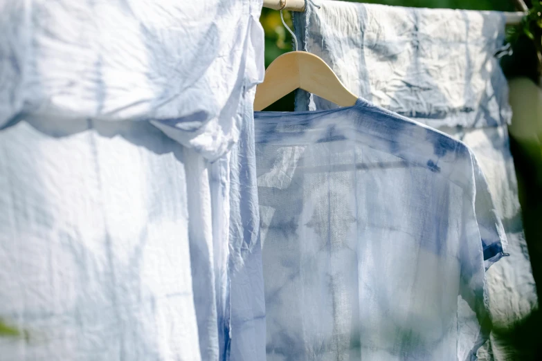a blue and white shirt hanging on a clothes line, inspired by Louise Bourgeois, trending on unsplash, process art, wearing translucent sheet, acid wash layering, moonlight grey, having fun in the sun