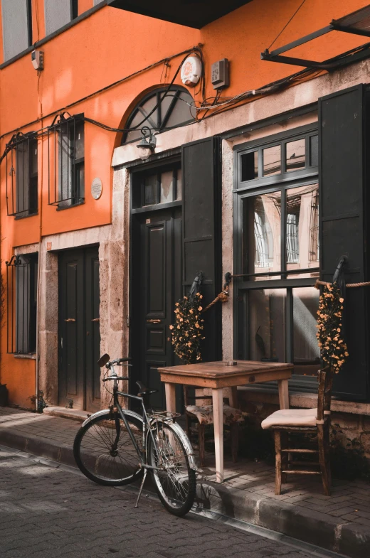 a bicycle parked in front of an orange building, pexels contest winner, renaissance, black and brown colors, holiday season, cafe tables, doorways