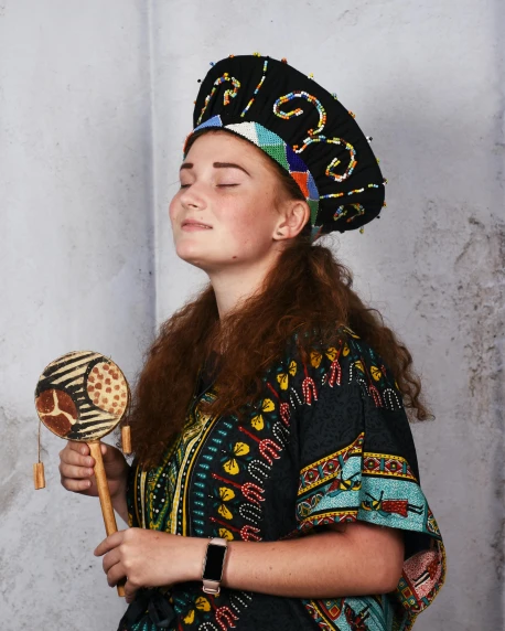 a woman standing in front of a white wall holding a brush, unsplash, renaissance, holding maracas, ornate turban, sadie sink, baggy clothing and hat