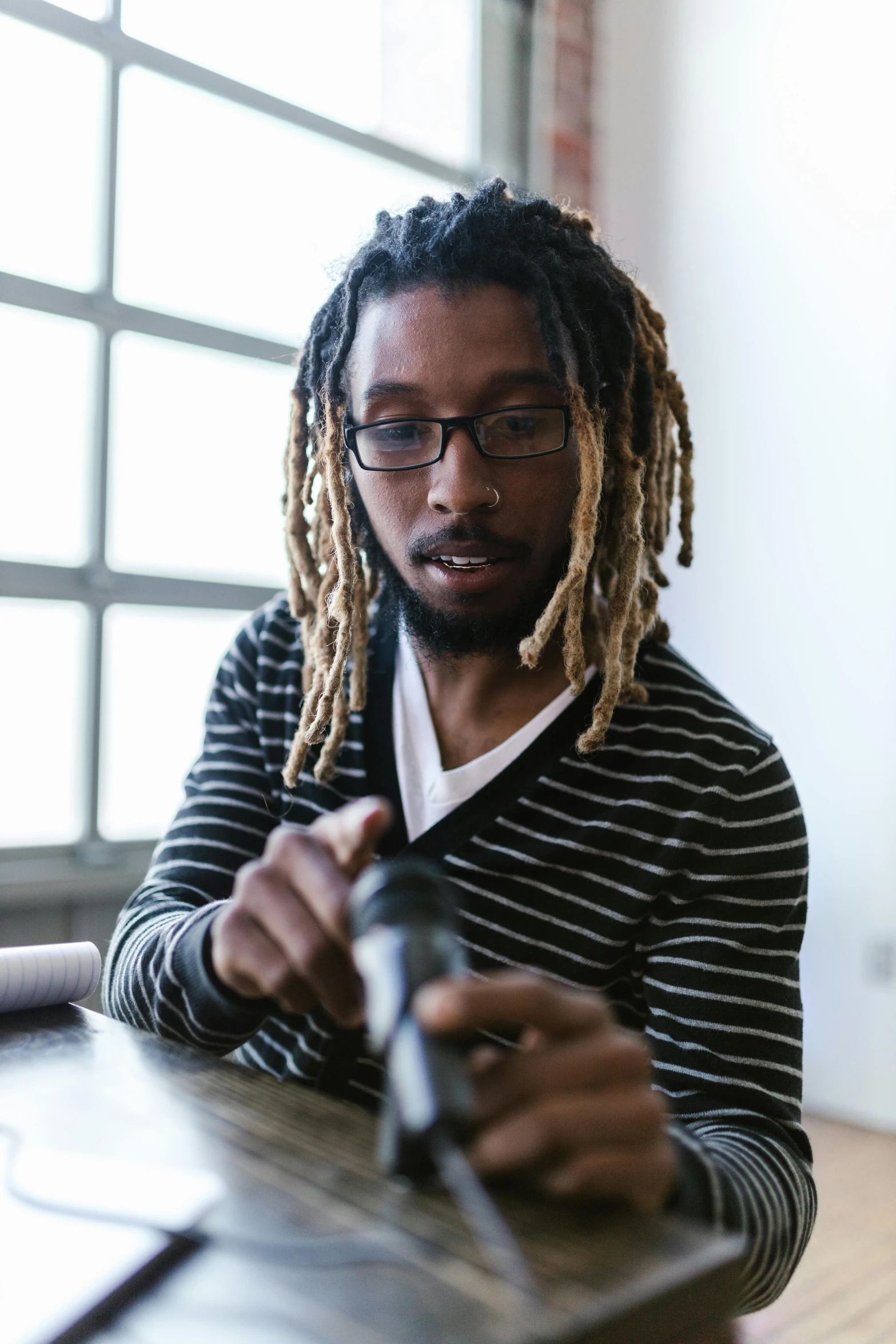 a man with dreadlocks sitting at a table, pexels contest winner, black arts movement, holding an activated lightsaber, man with glasses, adafruit, loosely cropped