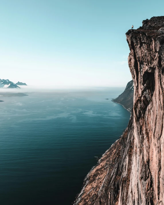 a person standing on the edge of a cliff, by Johannes Voss, pexels contest winner, mountains and oceans, towering above a small person, rock climbing, beautiful panoramic imagery