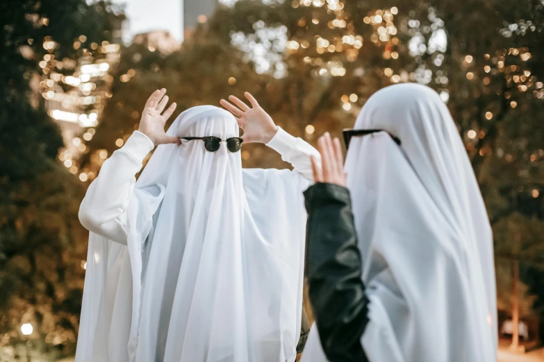 a couple of people that are standing in the grass, an album cover, trending on unsplash, hurufiyya, halloween ghost under a sheet, white hijab, sunglasses and a scarf, cosplay photo