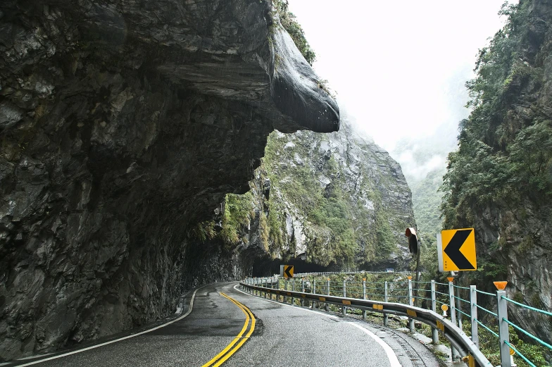 there is a yellow and black sign on the side of the road, by Peter Churcher, pexels contest winner, inside a gorge, ben lo, large overhangs, dashcam footage