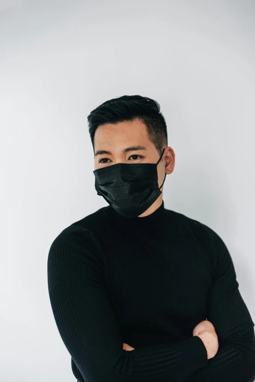 a man standing with his arms crossed wearing a black face mask, inspired by Russell Dongjun Lu, on a gray background, wearing a black sweater, profile image, cliff chiang