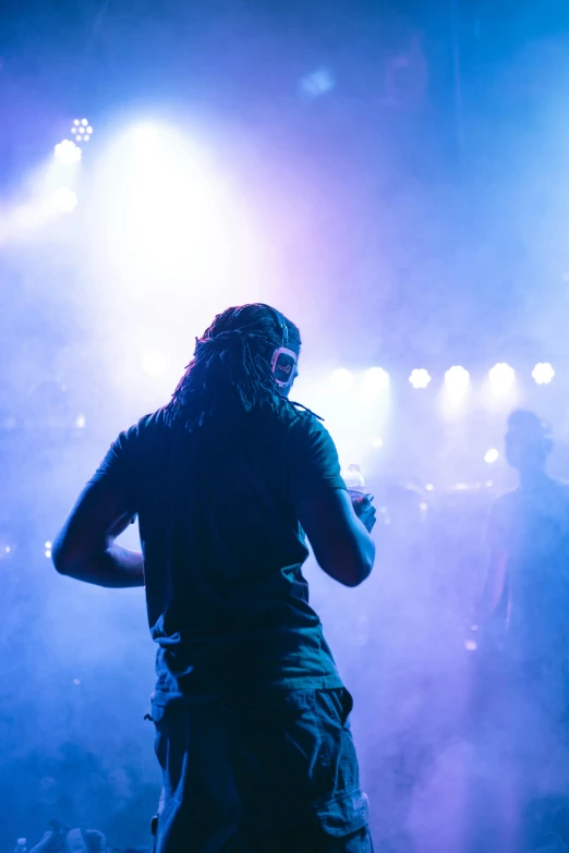 a man standing on top of a stage holding a microphone, pexels contest winner, happening, dreads, dj at a party, facing away, hazy