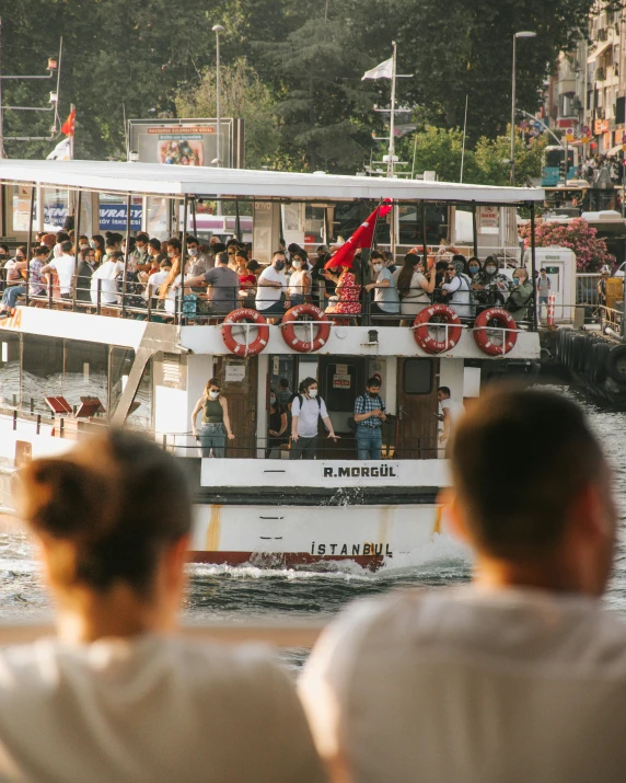 a group of people sitting on top of a boat, in front of a large crowd, istanbul, 🚿🗝📝