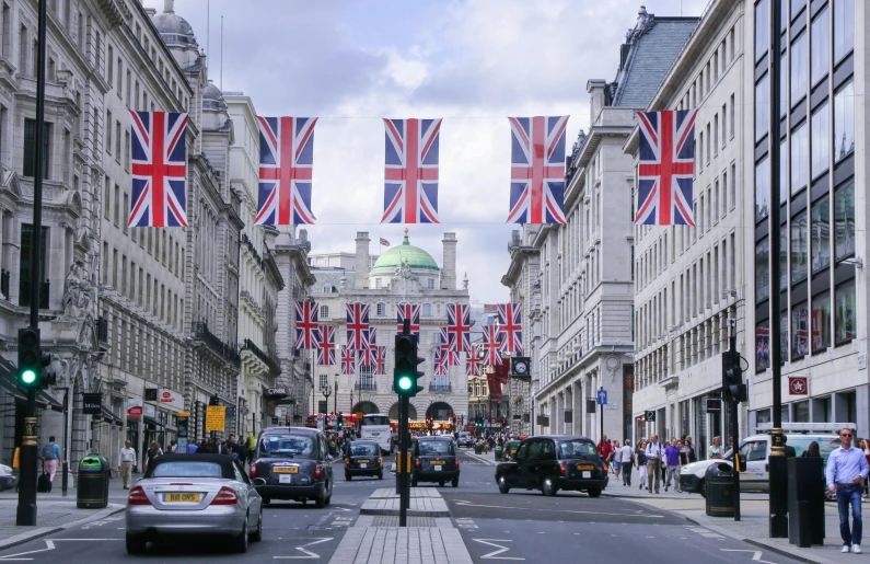 a street filled with lots of traffic next to tall buildings, an album cover, shutterstock, renaissance, united kingdom flags, square, on a great neoclassical square, uk