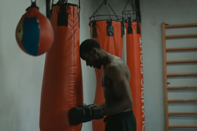 a man standing next to a punching bag, pexels contest winner, happening, man is with black skin, high quality screenshot, orange gi, as well as scratches