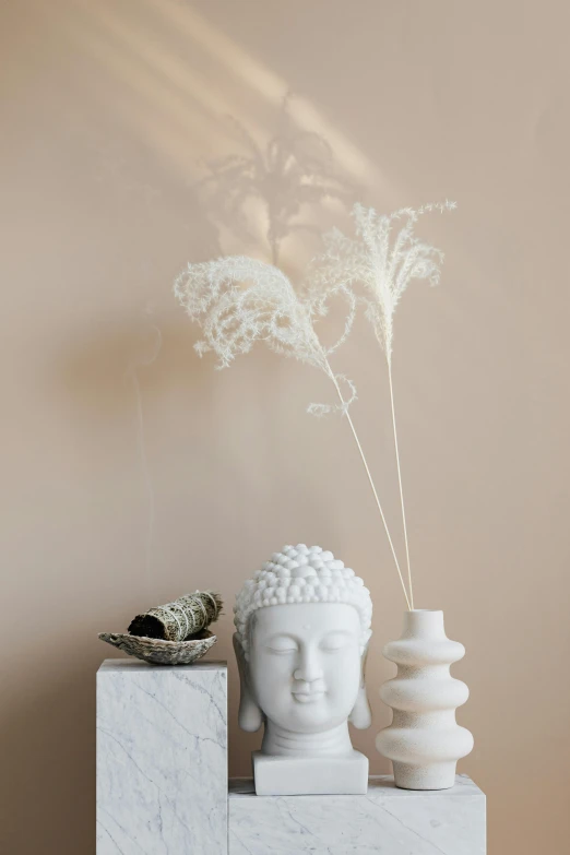 a white statue sitting on top of a table next to a vase, trending on pexels, light and space, plume made of seaweed, lacey accessories, studio shot, buddhist