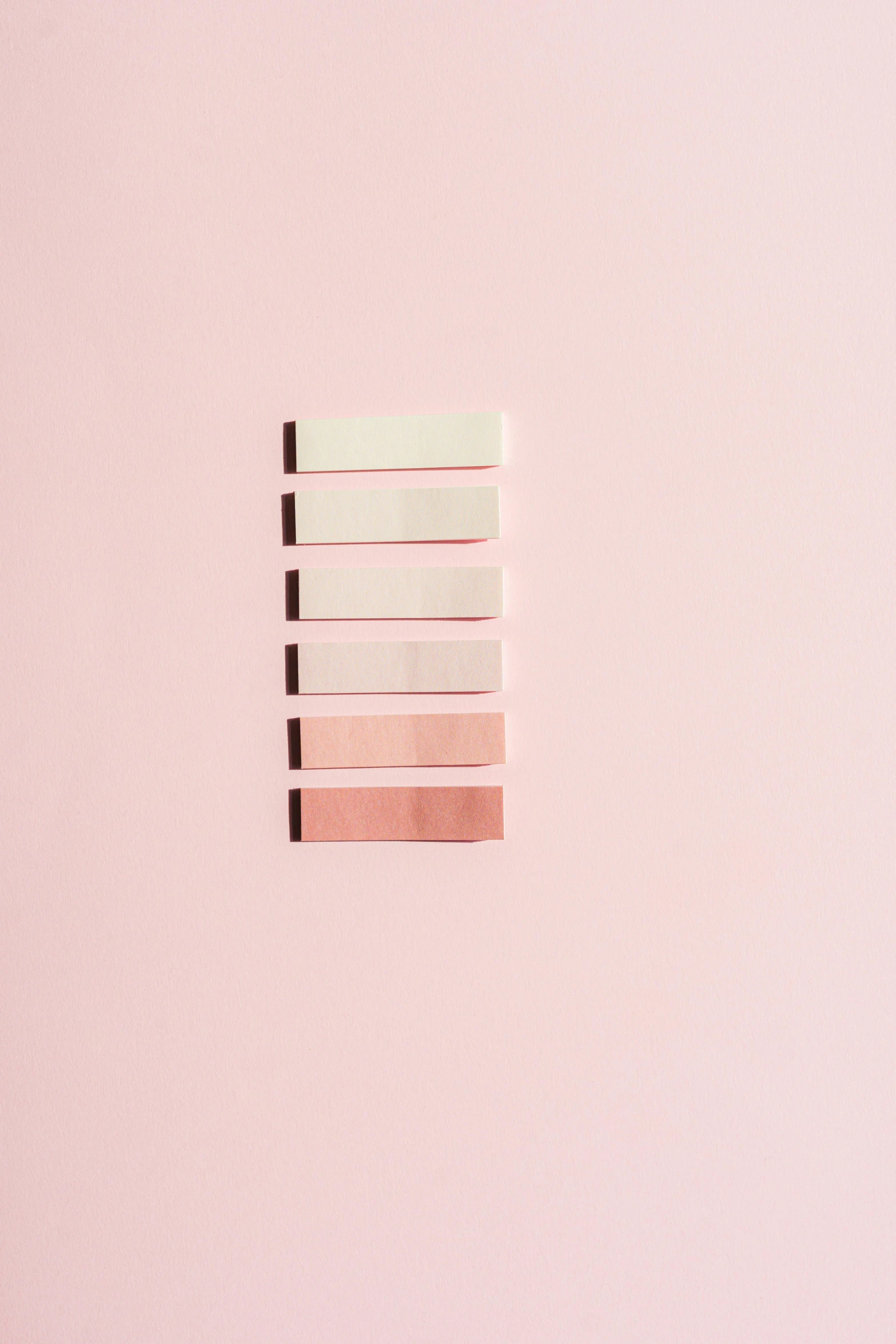 a close up of a piece of paper on a pink surface, ivory and copper, lined up horizontally, 6 colors, beautiful image