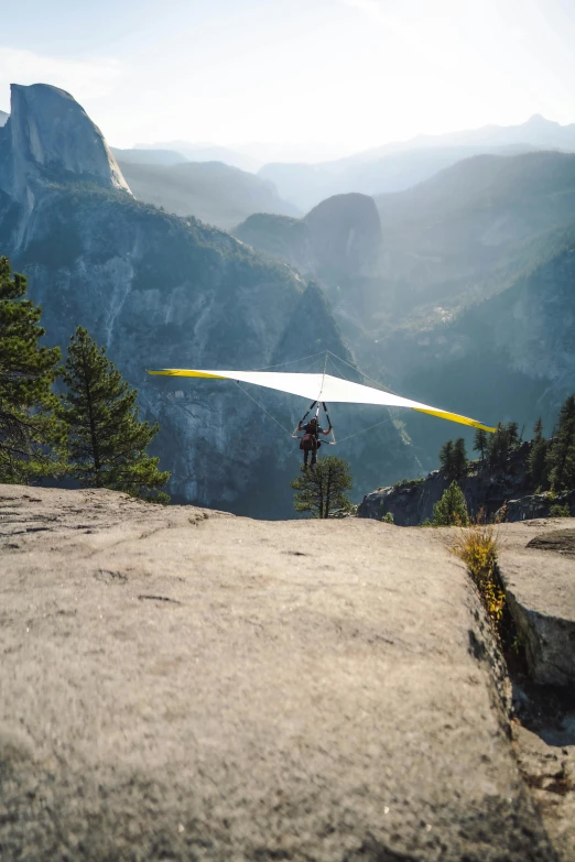 a man flying a hang glider on top of a mountain, by Jessie Algie, yosemite, 8k ultra, national geographics, outside on the ground