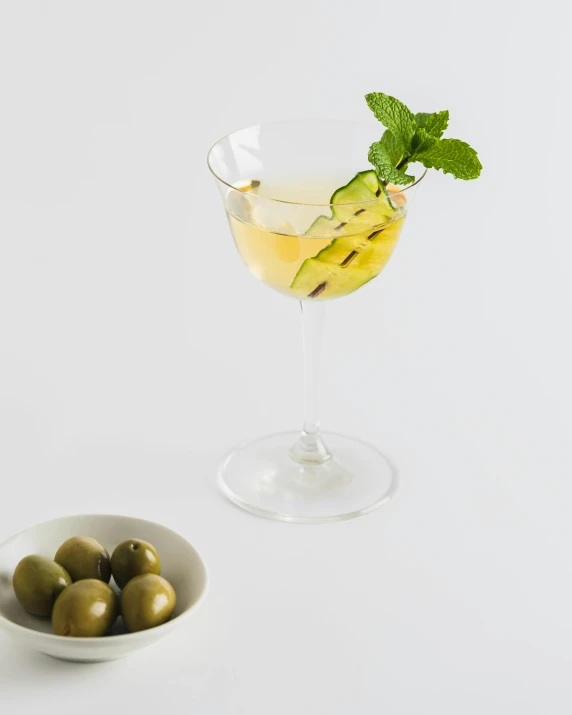 a glass of wine next to a bowl of olives, inspired by Ndoc Martini, product view, cucumber, square, mint