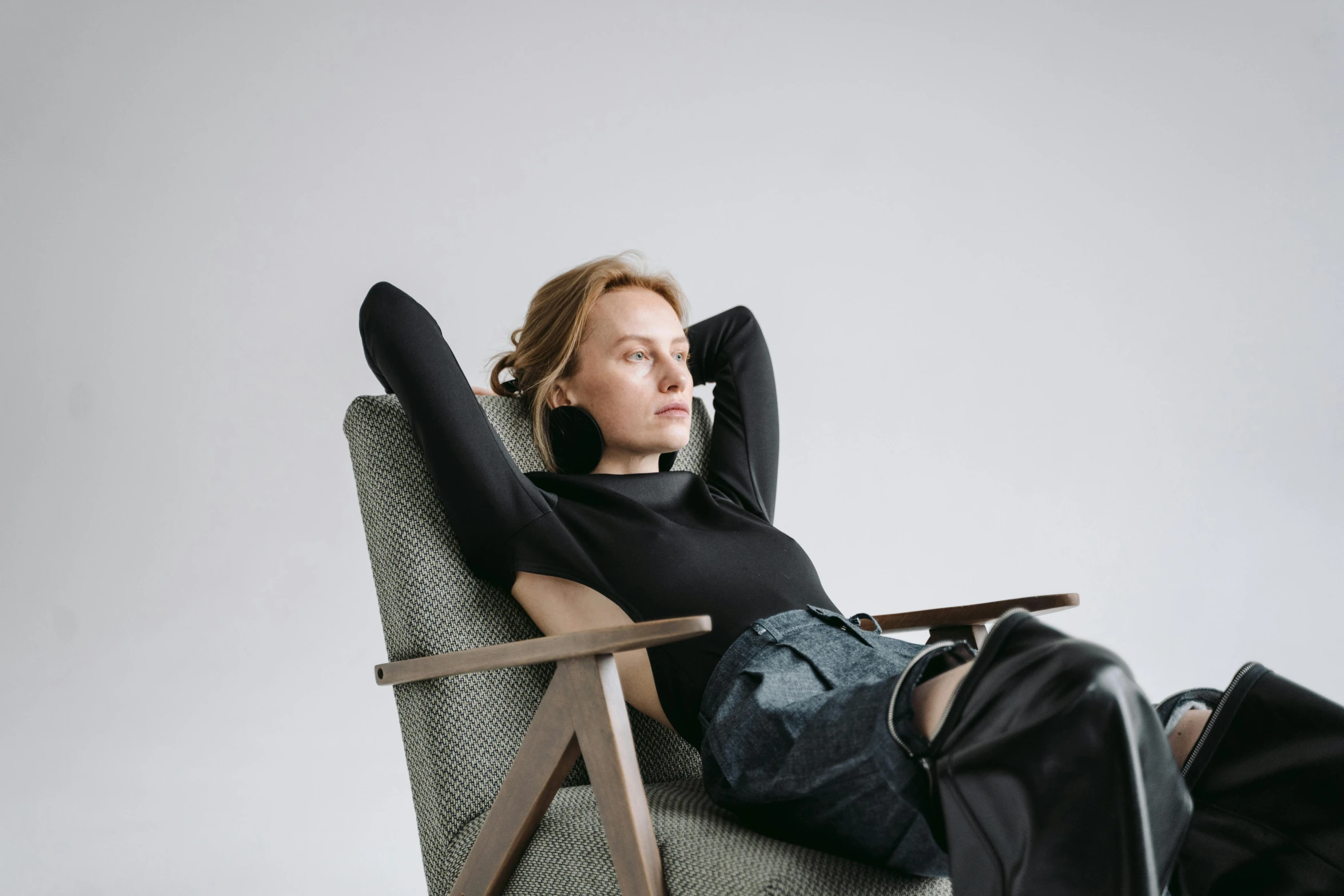 a woman sitting in a chair with her hands behind her head, a portrait, inspired by Constantin Hansen, trending on unsplash, wearing a black sweater, various posed, designer product, reclining