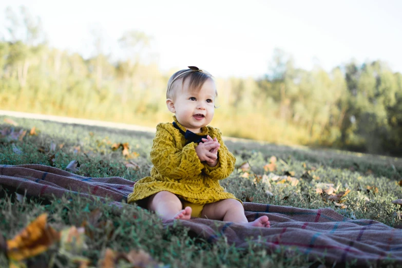 a baby girl sitting on a blanket in the grass, a portrait, unsplash, fall season, portrait n - 9, portrait image