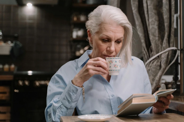 a woman sitting at a table drinking from a cup, pexels contest winner, a silver haired mad, reading, avatar image, handsome