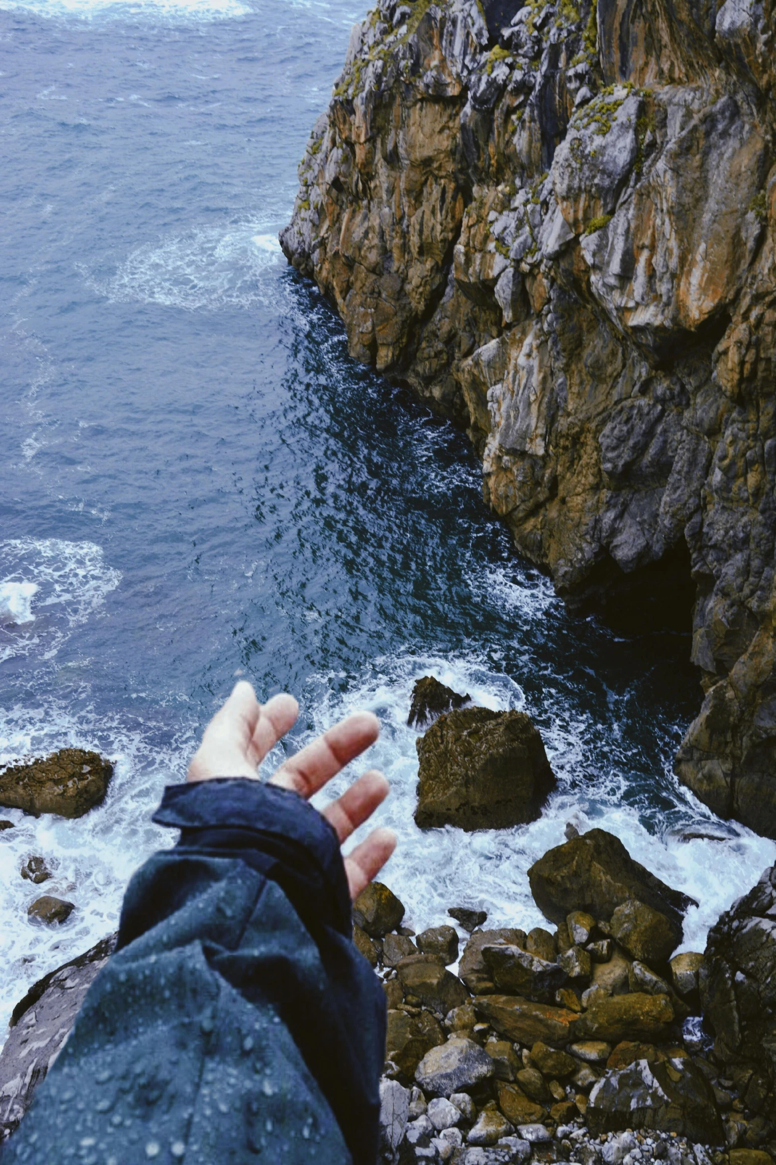 a person standing on top of a rocky cliff next to the ocean, open hand, looking down from above, instagram post, wet rocks