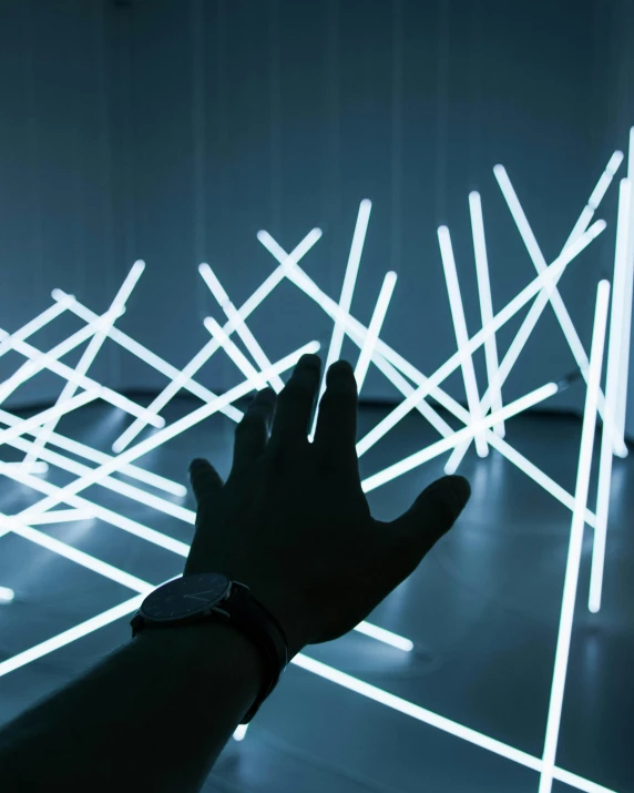 a person standing in front of a light sculpture, inspired by Ryoji Ikeda, unsplash, interactive art, closeup of hand, glow sticks, geometric lines, trending on dezeen
