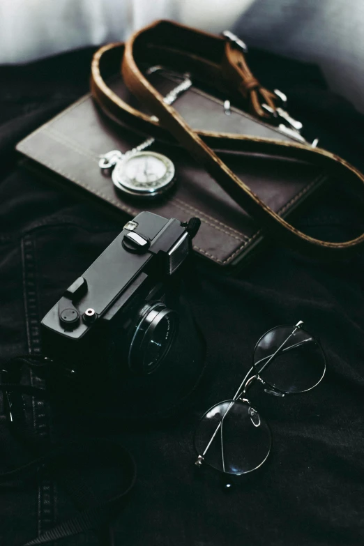 a camera sitting on top of a bed next to a pair of glasses, pexels contest winner, minimalism, leather straps, black on black, vintage photo, jewelry