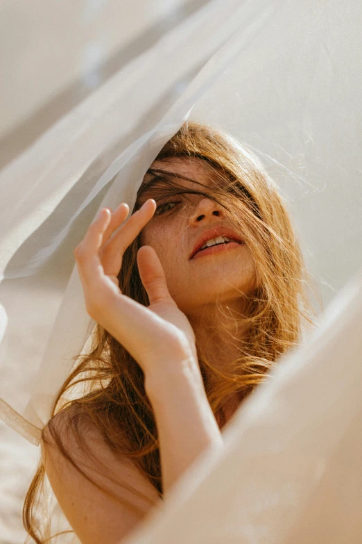 a woman holding a veil over her face, by irakli nadar, trending on unsplash, renaissance, white cloth in wind shining, brown flowing hair, sunny light, curtain bangs