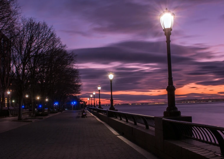 a bench sitting on top of a sidewalk next to a body of water, by Chris Rallis, pexels contest winner, romanticism, streetlamps, purple sunset, upon a peak in darien, new york city