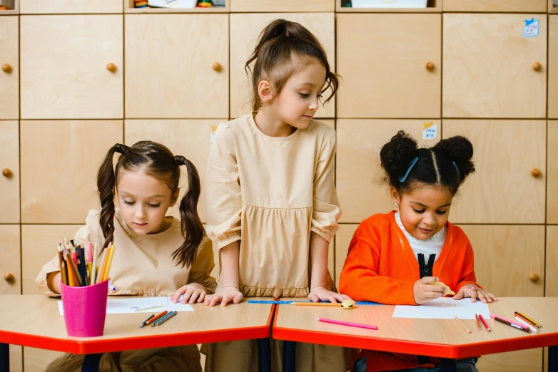 three little girls sitting at a table with pencils, trending on pexels, standing in class, idealised, brown hair in two buns, alana fletcher