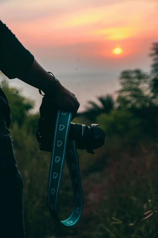 a person holding a camera with a sunset in the background, straps, high quality image”, trending photo, waist high