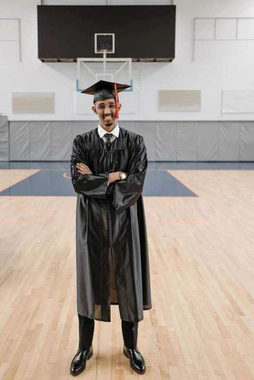 a man in a graduation gown standing on a basketball court, by Bernie D’Andrea, on grey background, riyahd cassiem, commercially ready, standing in class