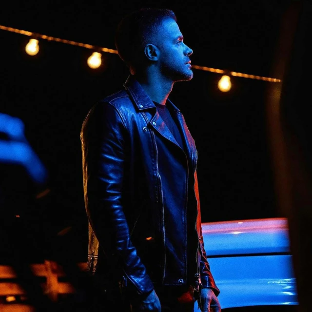 a man in a leather jacket standing next to a car, extremely moody blue lighting, singer maluma, profile image, tyler durden