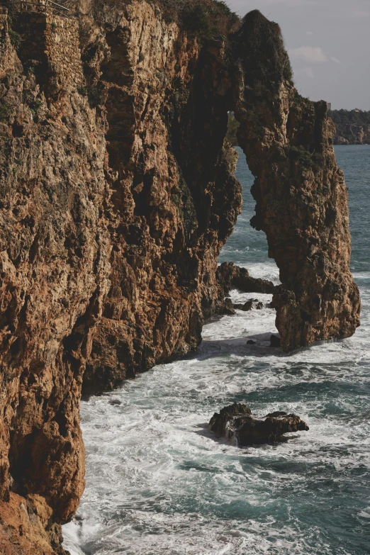 a man standing on top of a cliff next to the ocean, pexels contest winner, renaissance, rock arches, portugal, texture, middle close up composition