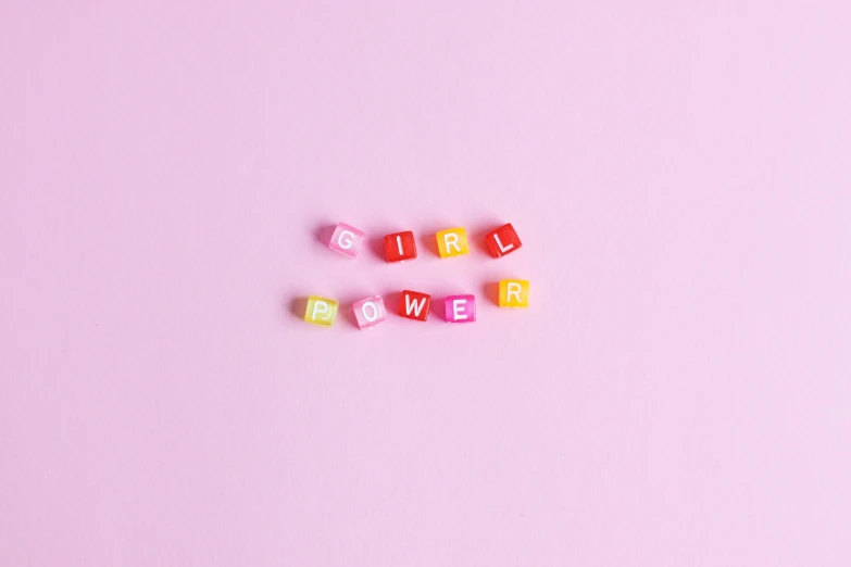 a couple of dice pieces sitting on top of a pink surface, feminist art, power girl, word, made out of legos, candy pastel